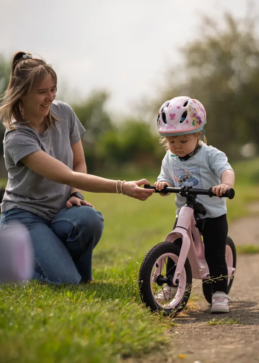 A toddler on a pink Shyre Myndie balance bike with a parent