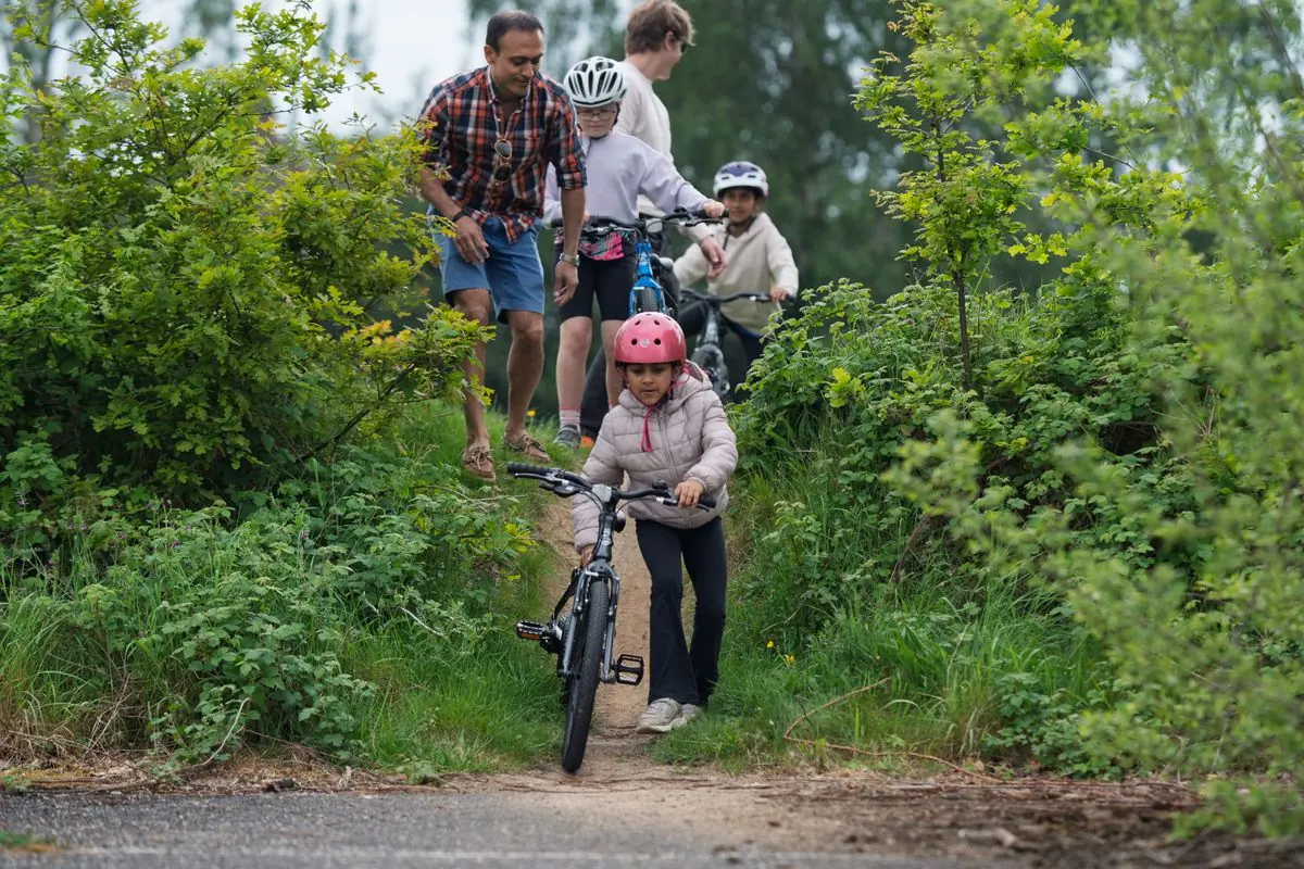 A family walking their bikes along a woodland trail
